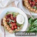 Bowl of pesto risotto topped with cherry tomatoes, sliced sausage and burrata cheese