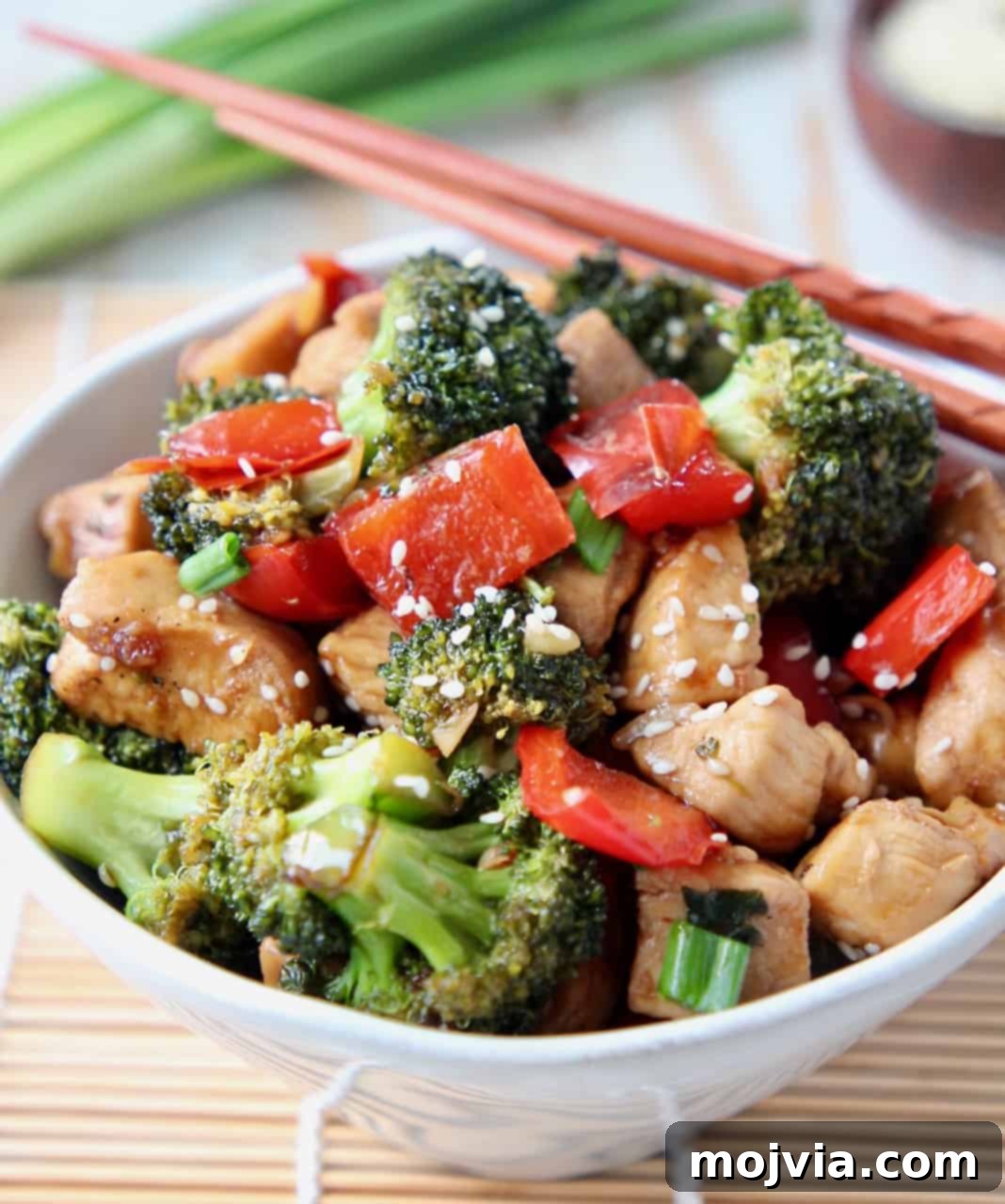 Teriyaki chicken and broccoli stir fry in a white bowl with chopsticks on the side, ready to be enjoyed.