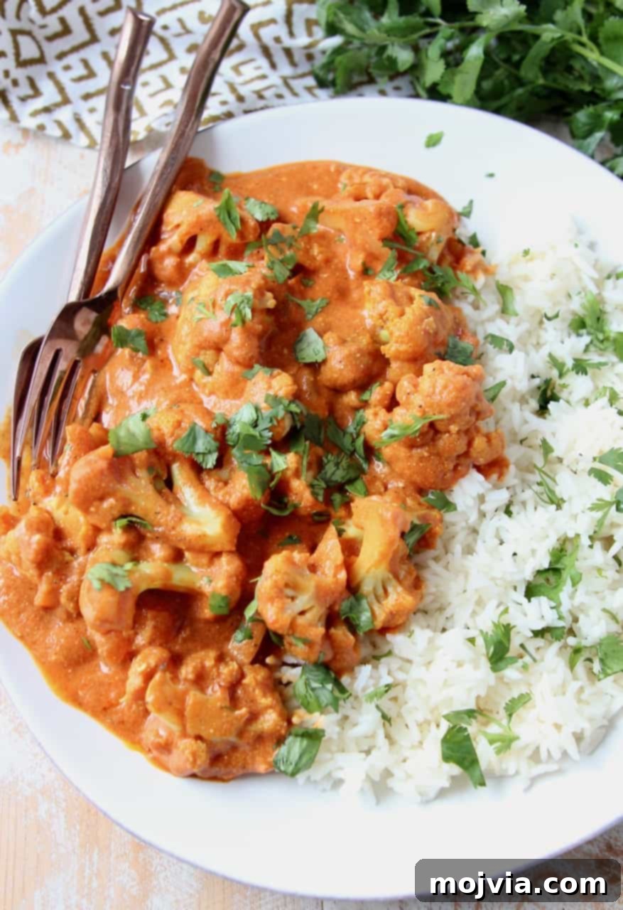 Creamy Indian Butter Cauliflower Curry 5 Cauliflower curry on a plate with rice, garnished with cilantro, and accompanied by forks