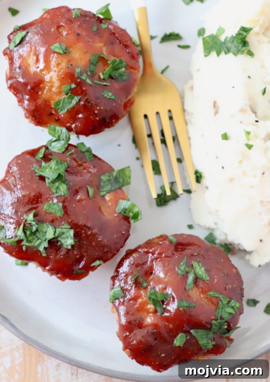 Glazed mini BBQ meatloaves served on a plate with a fork and a generous portion of mashed potatoes.
