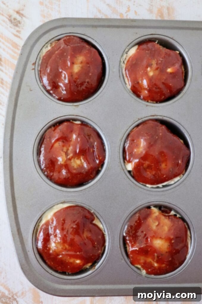 Mini meatloaves glazed with BBQ sauce, baking in a muffin tin to caramelized perfection.