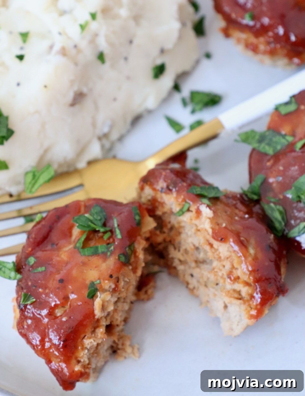 A mini meatloaf sliced in half on a plate, served with a fork and fluffy mashed potatoes.