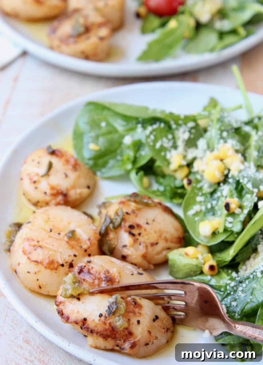 Grilled Scallops with Zesty Jalapeño-Lemon Butter 5 A fork gently slices into a perfectly cooked grilled scallop on a white plate, highlighting its tender, opaque interior. It's garnished with fresh herbs.