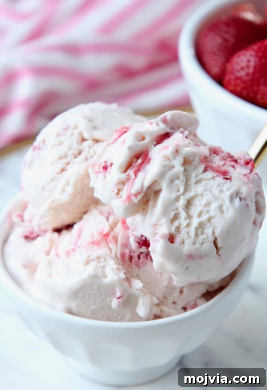 Scoops of strawberry ice cream in white bowl, garnished with fresh mint