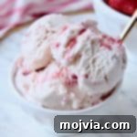 Scoops of strawberry ice cream in white bowl with gold spoon