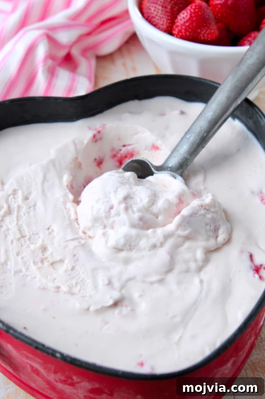 A scoop of homemade strawberry ice cream being lifted from a metal pan