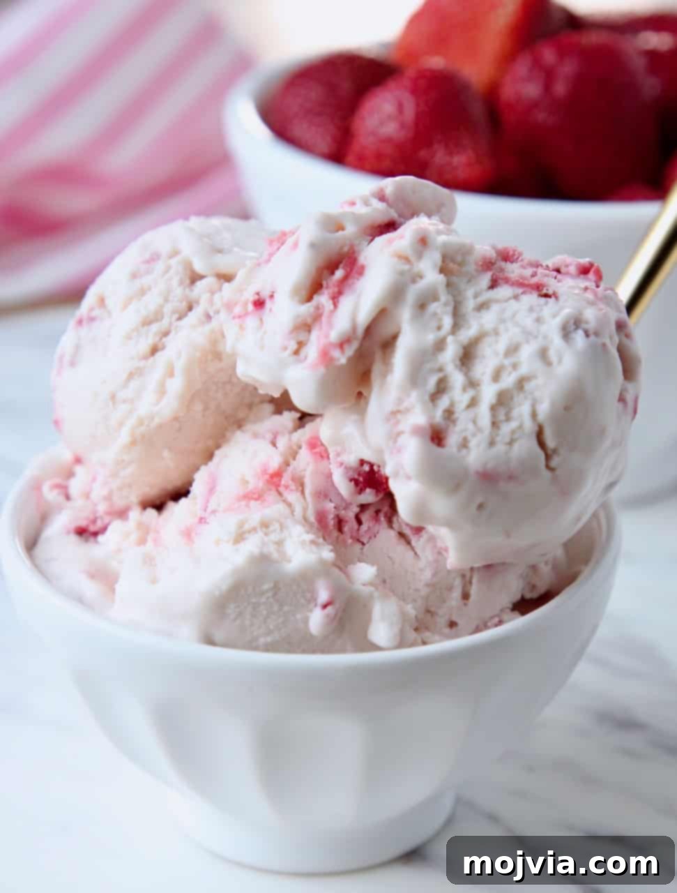 Scoops of strawberry ice cream in white bowl with a golden spoon
