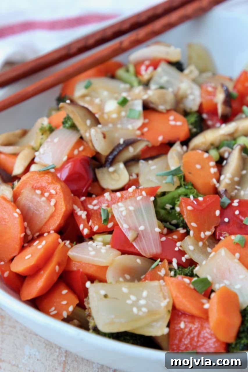 Sticky Soy-Ginger Roasted Asian Vegetables 2 A bowl of vibrant oven roasted Asian vegetables, garnished with sesame seeds and green onions, with chopsticks resting on the side.