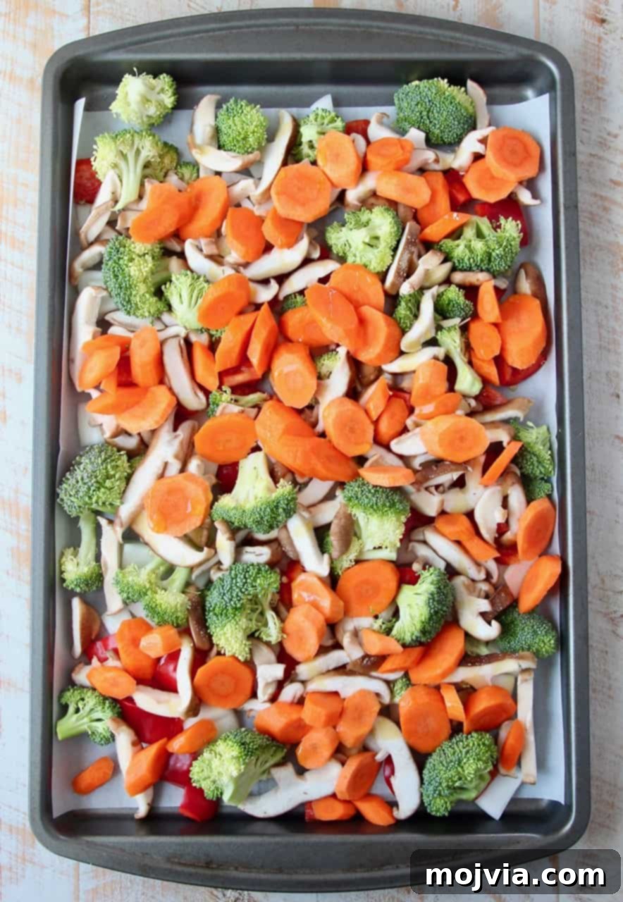 Sticky Soy-Ginger Roasted Asian Vegetables 4 Overhead image of chopped vegetables, including broccoli, carrots, bell peppers, onions, and mushrooms, spread out on a baking sheet, ready for roasting.