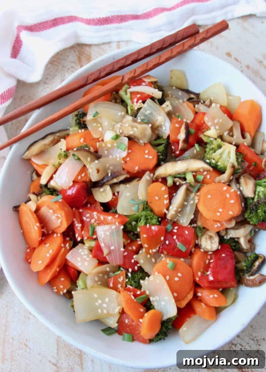 Sticky Soy-Ginger Roasted Asian Vegetables 5 Overhead image of a white bowl filled with glistening roasted Asian vegetables, garnished with sesame seeds and green onions, with chopsticks ready for serving.