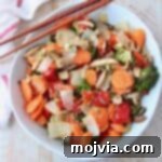 Overhead image of roasted Asian vegetables in white bowl with chopsticks on the side