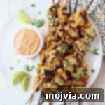 Savory Thai Chicken Satay with Creamy Peanut Sauce 7 Grilled chicken skewers on plate with bowl of peanut sauce on the side