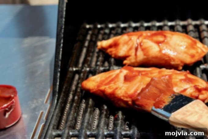10 Game-Changing Grilling Secrets 7 A delicious piece of chicken being brushed with BBQ sauce on the grill, illustrating the final step for perfect flavor.