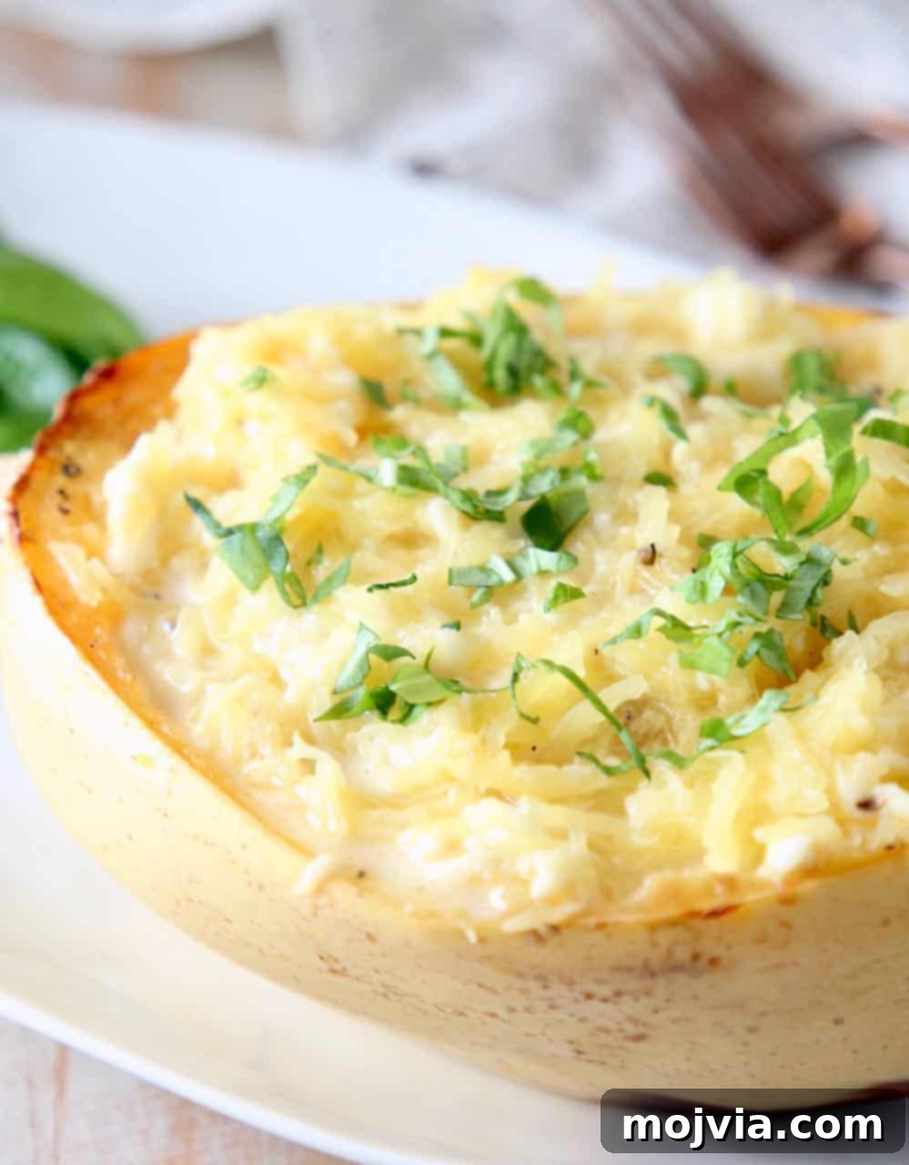 Golden Spaghetti Squash Mac and Cheese Bake 4 Half of a roasted spaghetti squash tossed in cheese sauce on white plate, garnished with fresh basil