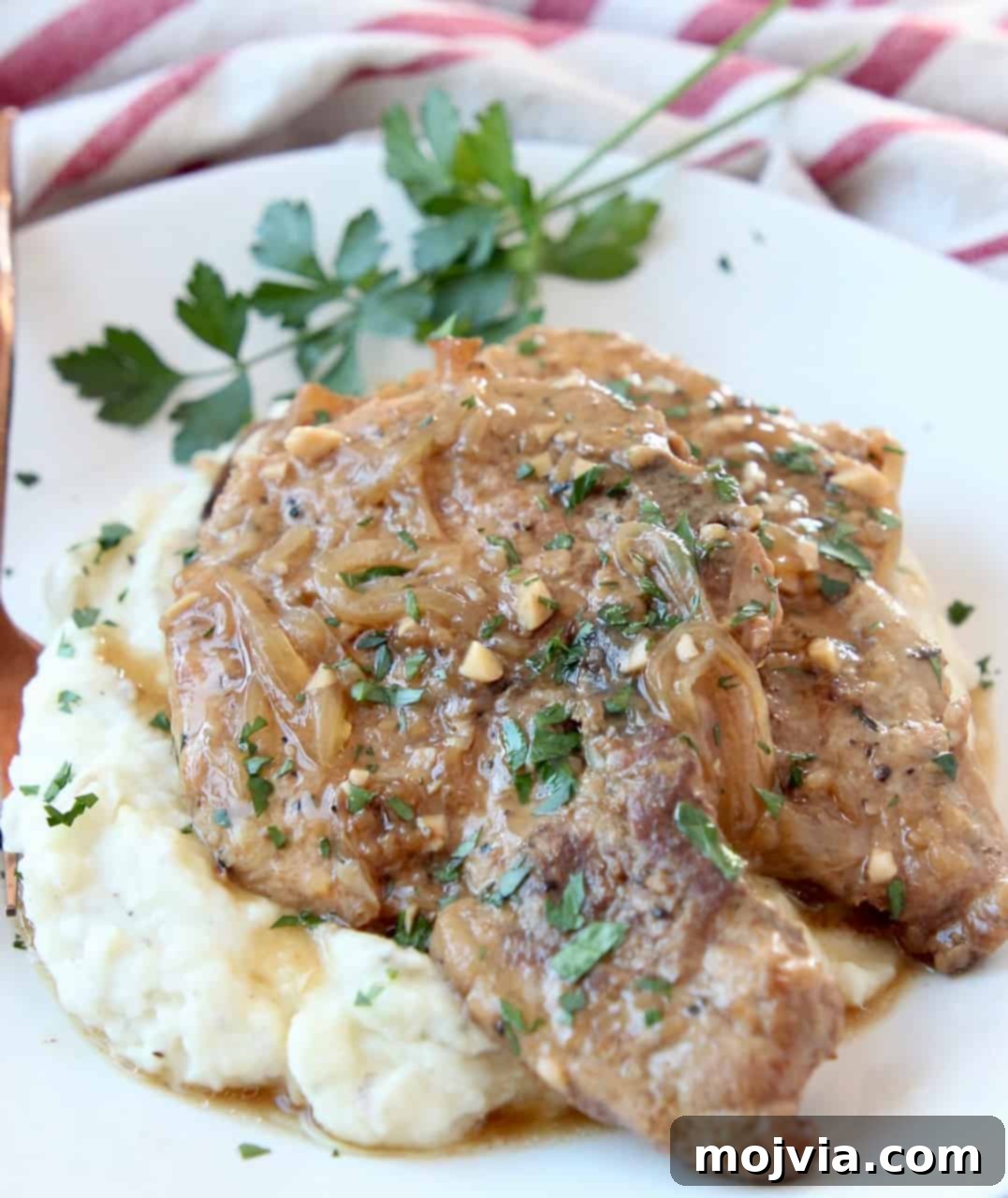 Slow Cooker French Onion Pork Chops 5 Two beautifully stacked tender Crock Pot Pork Chops on a plate with mashed potatoes, smothered in French onion gravy.