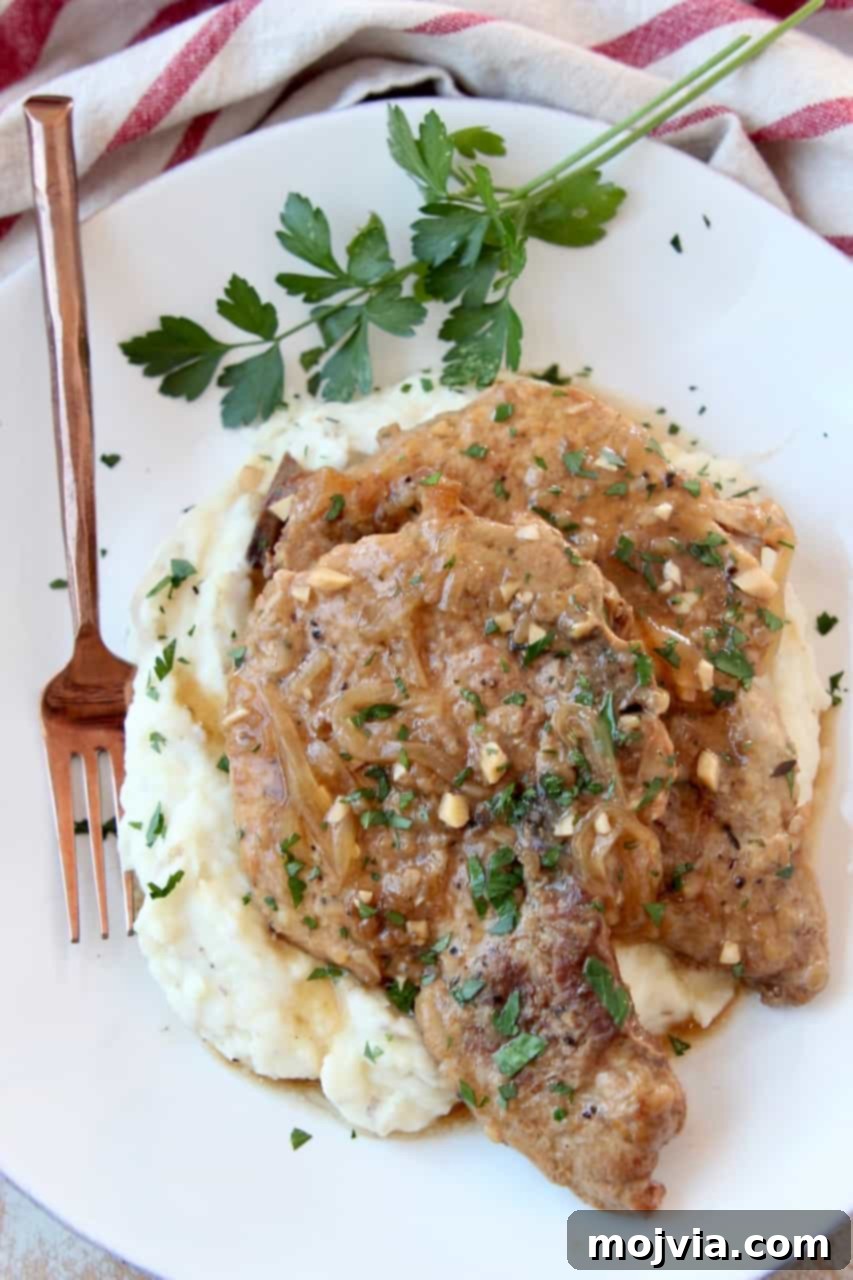 Slow Cooker French Onion Pork Chops 6 Overhead view of two French Onion Crock Pot Pork Chops on a plate with mashed potatoes and ample brown gravy, garnished with fresh herbs.