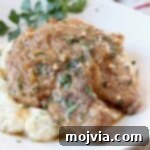 Two tender French Onion Crock Pot Pork Chops on a plate, covered with savory gravy, on top of creamy mashed potatoes.