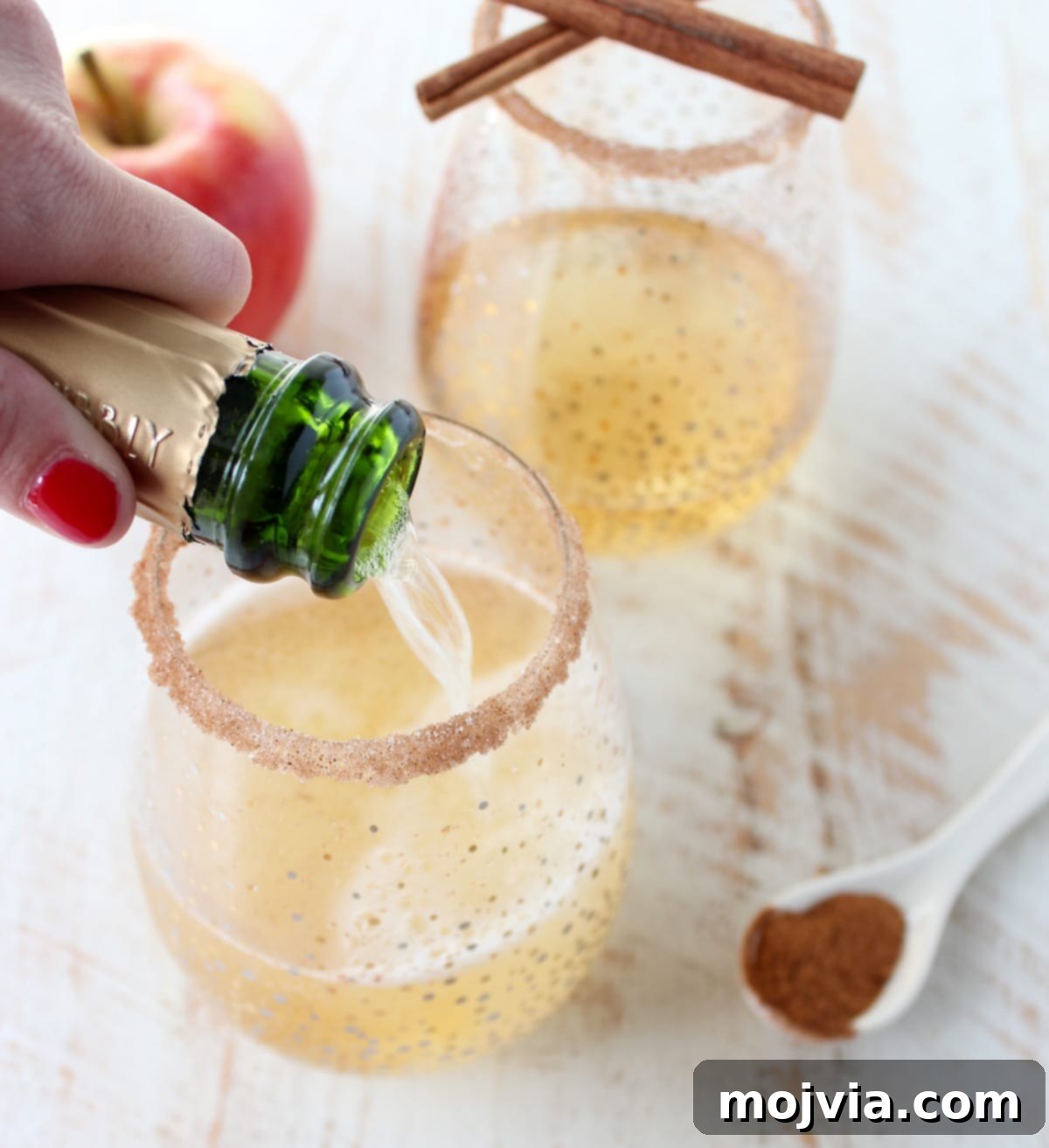 Crisp Apple Champagne Fizz 2 Champagne being poured into a stemless wine glass with a cinnamon sugar rim, highlighting the festive appeal of an apple cider champagne cocktail.