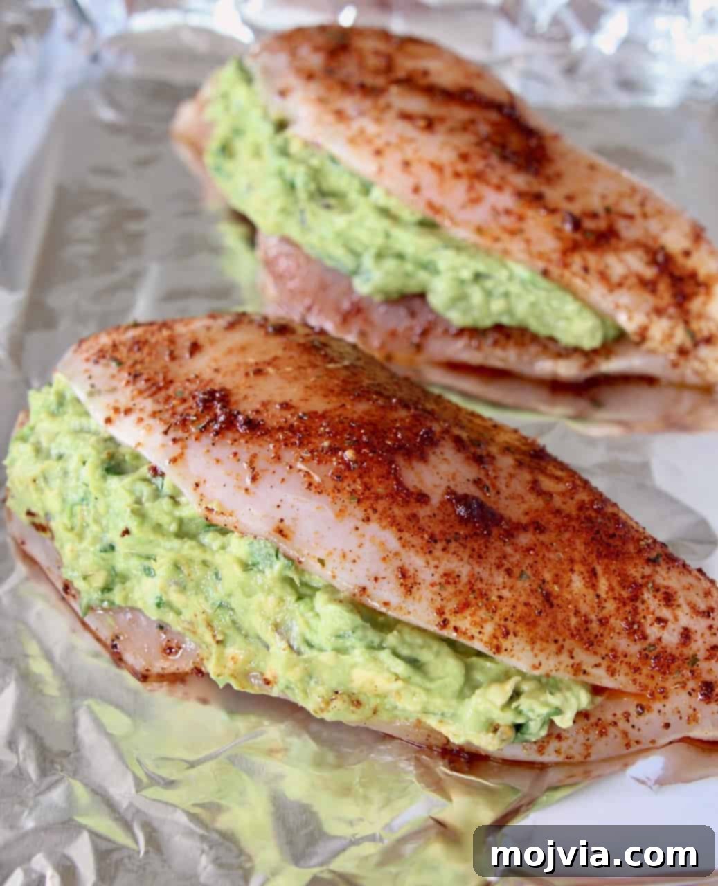 Uncooked guacamole stuffed seasoned chicken breasts on foil-lined baking sheet, ready for the oven