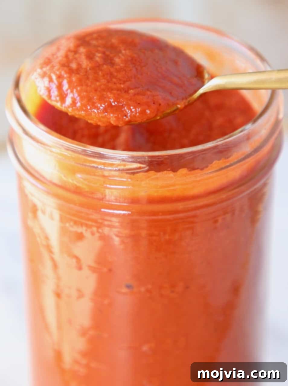 Classic Red Enchilada Sauce 6 spoon of enchilada sauce lifted out of mason jar of sauce