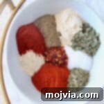 Bayou Blast Seasoning 5 Various spices and herbs artfully arranged in a white bowl, highlighted by a gold spoon, ready for a Cajun recipe.