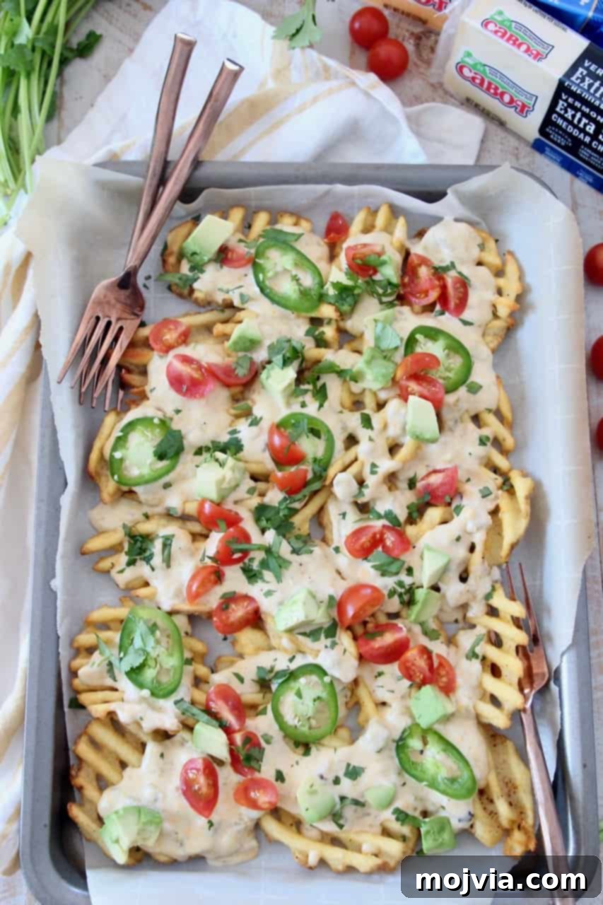 Loaded Waffle Nachos with Zesty Green Chili Cheese 2 Overhead shot of freshly baked Waffle Fry Nachos generously covered with melted Green Chili Cheese Sauce and various vibrant toppings, ready to be shared with forks.