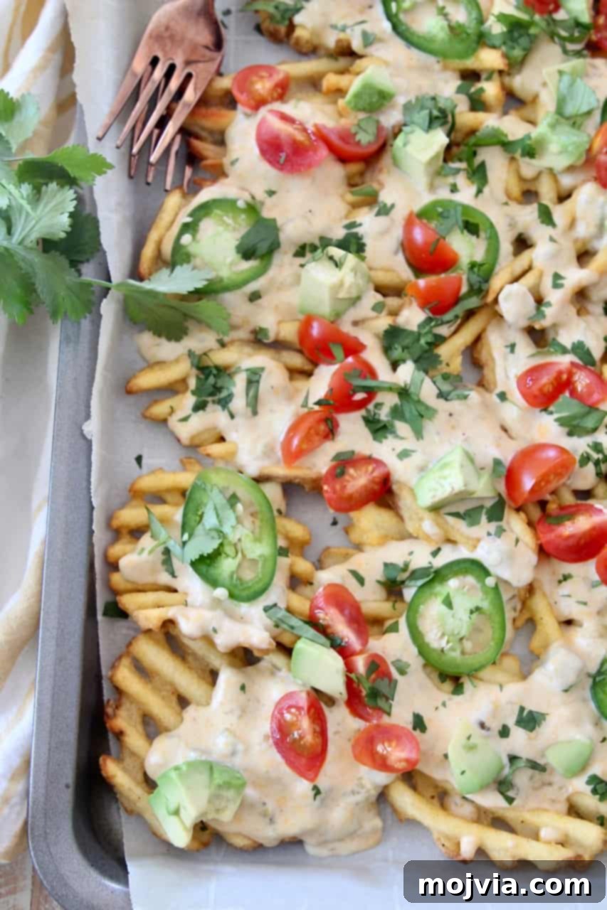 Loaded Waffle Nachos with Zesty Green Chili Cheese 4 Overhead view of crispy waffle fries arranged on a baking sheet, generously covered with a rich, melted cheese sauce, fresh from the oven.