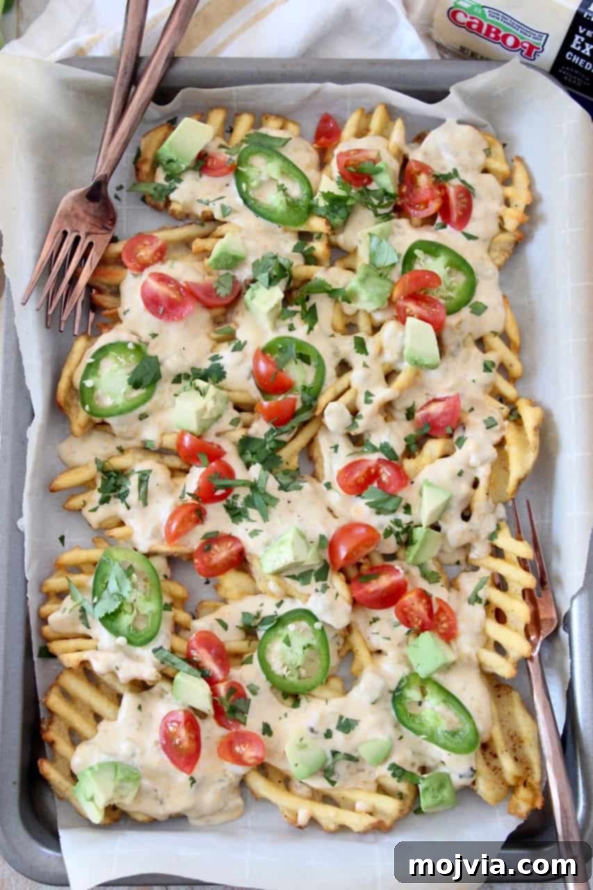 Loaded Waffle Nachos with Zesty Green Chili Cheese 5 Overhead image of a sheet pan filled with Waffle Fry Nachos, garnished with fresh toppings and accompanied by forks, inviting diners to share.
