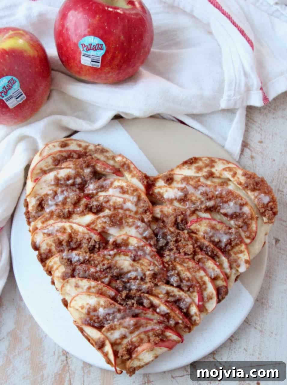 Cinnamon Streusel Apple Dessert Pizza 2 Overhead image of a heart-shaped apple dessert pizza on a serving dish with fresh apples on the side, highlighting its appealing presentation.