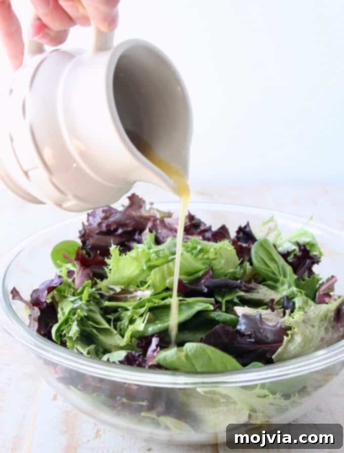 Bright Fuji Apple Dressing 5 Small pitcher pouring homemade vinaigrette dressing on a fresh salad in a glass bowl
