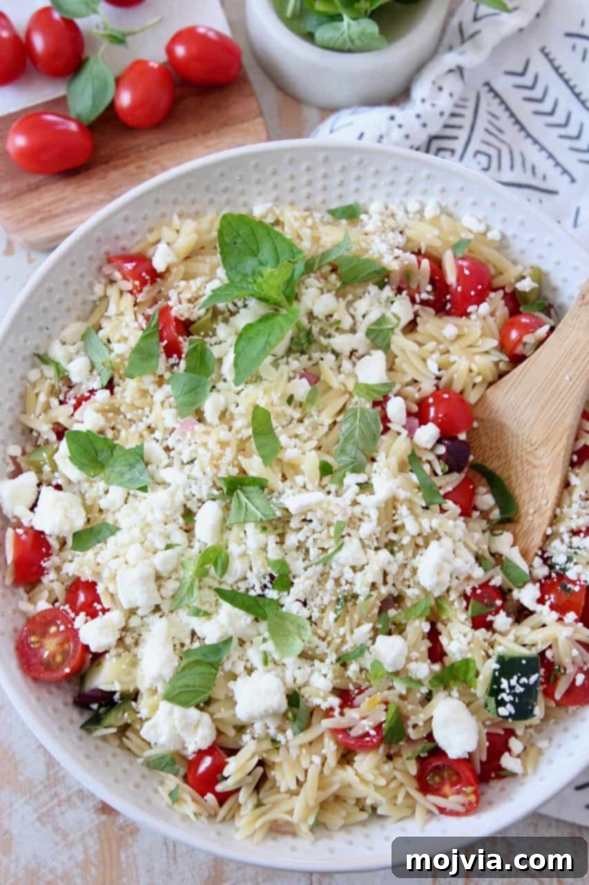 Bright Mediterranean Orzo Salad 2 A bowl of vibrant Greek orzo salad with a wooden spoon, garnished with fresh herbs.