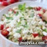 Greek Orzo Salad in a white bowl, garnished with tomatoes, mint, and feta.