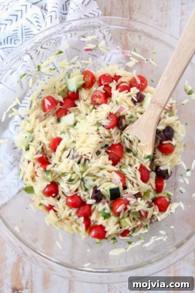 Bright Mediterranean Orzo Salad 7 Greek Orzo Salad in a large glass bowl with a wooden spoon, showing all ingredients combined.