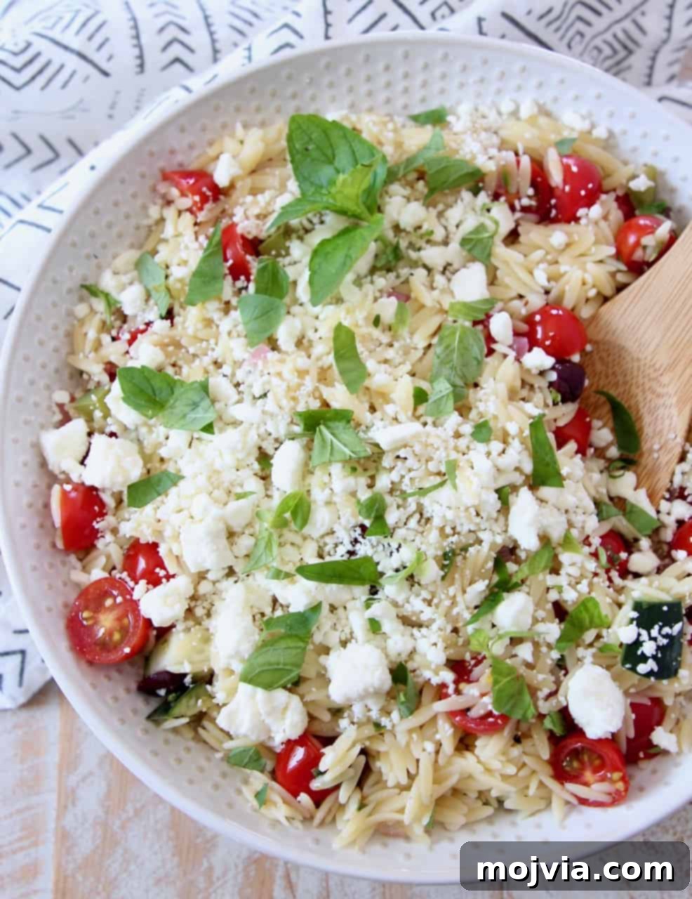 Bright Mediterranean Orzo Salad 10 A serving of Greek Orzo Salad with vibrant tomatoes and crumbled feta, served in a white bowl with a wooden spoon.