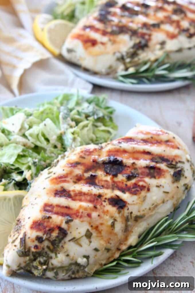Bright Lemon & Rosemary Chicken 5 Grilled lemon rosemary chicken breast on a plate with fresh salad, garnished with a sprig of rosemary and lemon wedge