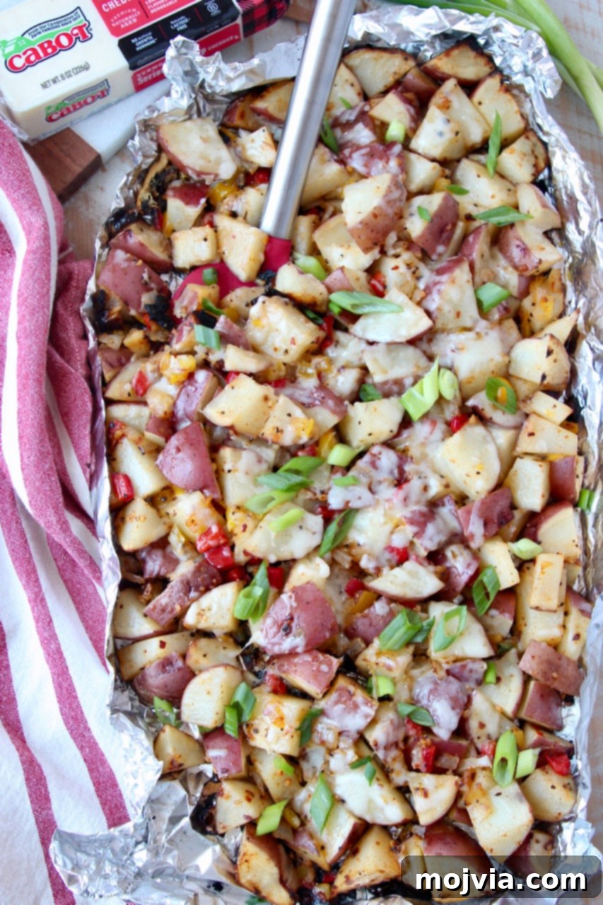 Golden Cheesy Grilled Potatoes 2 Grilled diced potatoes in foil with spatula, topped with melted cheese and fresh green onions