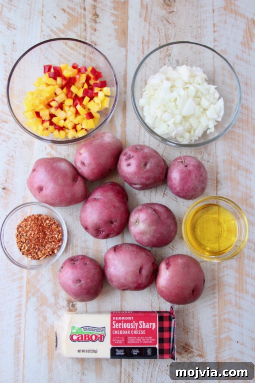 Golden Cheesy Grilled Potatoes 3 Ingredients for cheesy grilled potatoes laid out on a cutting board: red potatoes, bell peppers, onions, olive oil, steak seasoning, and a block of cheddar cheese.