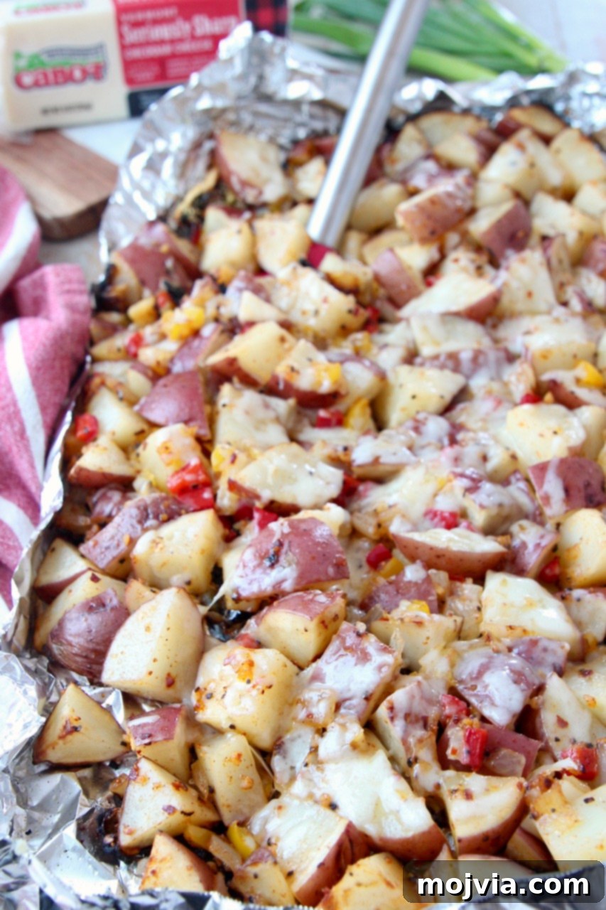 Golden Cheesy Grilled Potatoes 7 Cheesy grilled cubed potatoes in foil with a spatula, ready to be served.