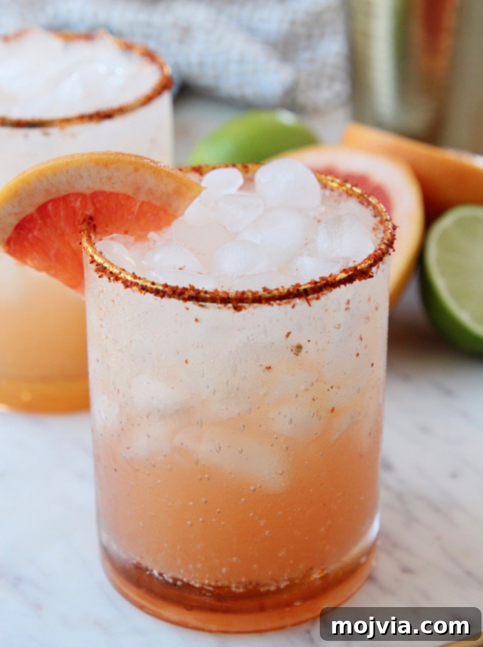 Whispers of Paloma 2 Paloma cocktail in a glass with a Tajin rim, garnished with a grapefruit wedge, set against a bright background