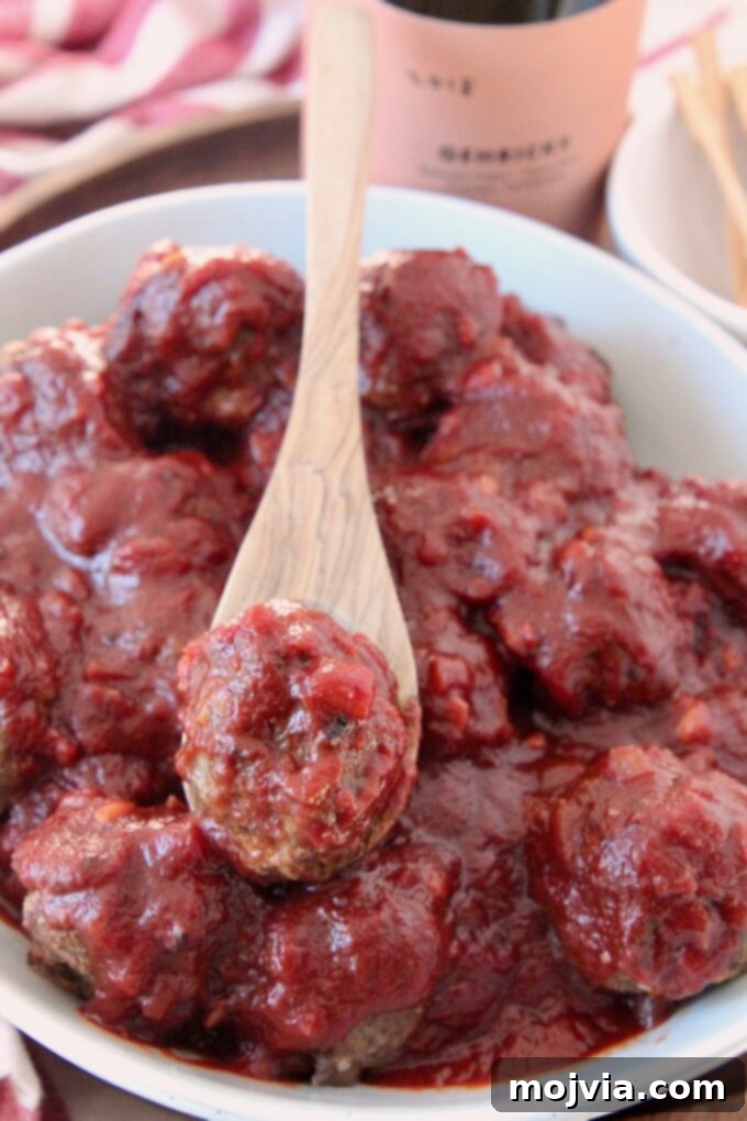 Red Wine Infused BBQ Beef Meatballs 6 meatball covered in bbq sauce on spoon in bowl of meatballs