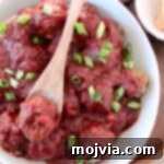bbq meatballs in bowl with wooden spoon topped with diced green onions