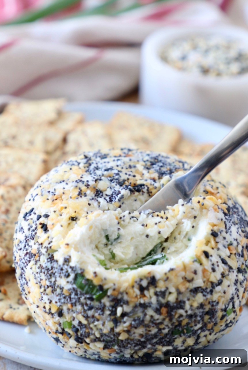 Everything Bagel Cheddar Party Ball 2 cheese ball with cheese spreader in the ball on plate with crackers