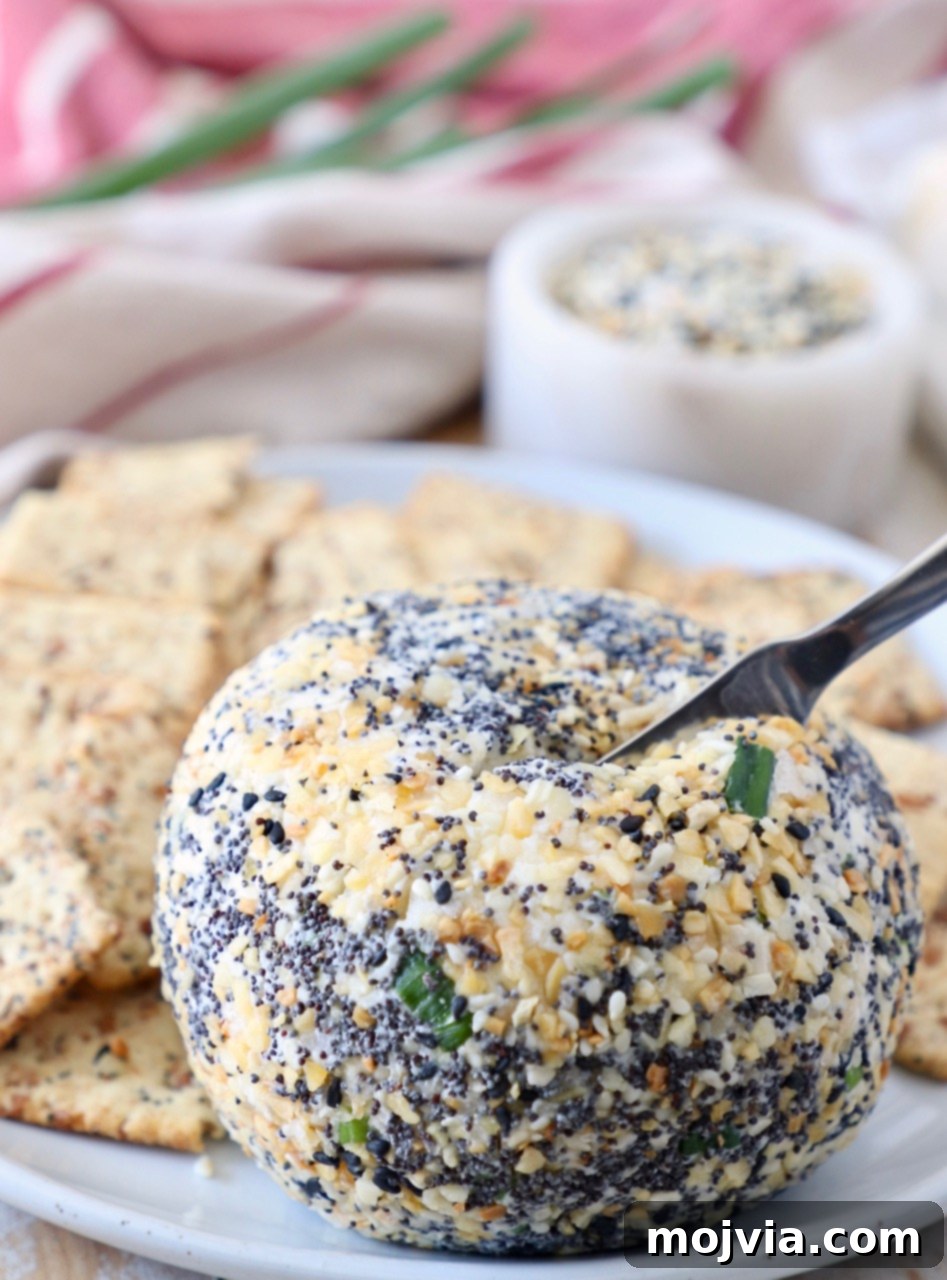 Everything Bagel Cheddar Party Ball 7 cheese ball on plate with spreader stuck in the cheese ball
