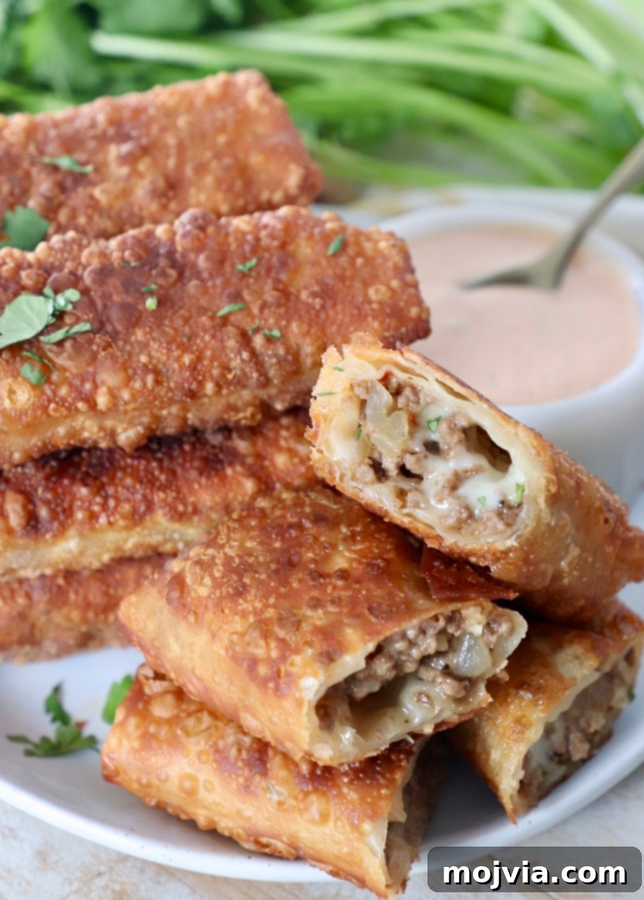 Crispy Cheeseburger Egg Rolls Air Fryer Pan Fry 2 cheeseburger egg rolls stacked up on plate with side of thousand island dressing in white bowl