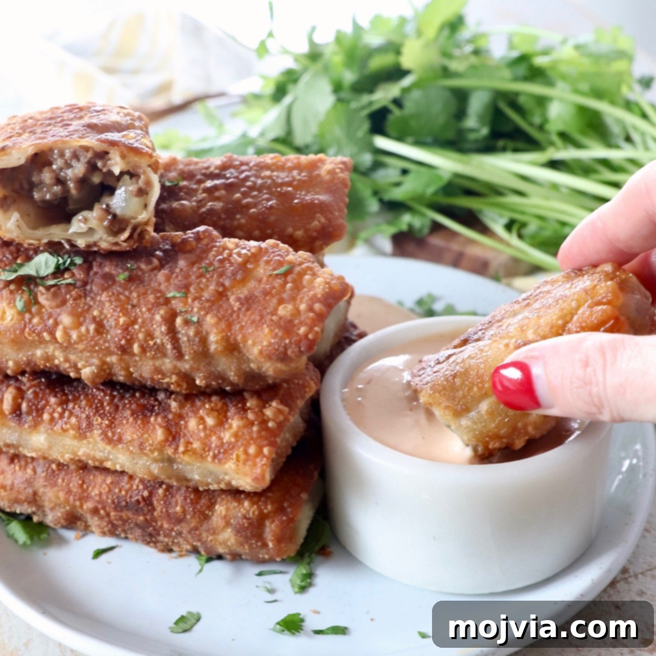 Crispy Cheeseburger Egg Rolls Air Fryer Pan Fry 8 hand dipping cheeseburger egg roll into sauce in bowl