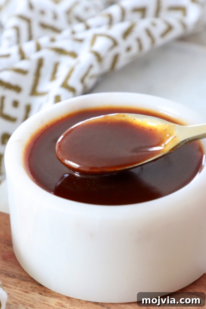 Perfect Stir-Fry Sauce 2 A small white bowl filled with glossy, rich brown stir fry sauce, with a gold spoon delicately dipped into the sauce, ready to be drizzled over a delicious stir-fry masterpiece.