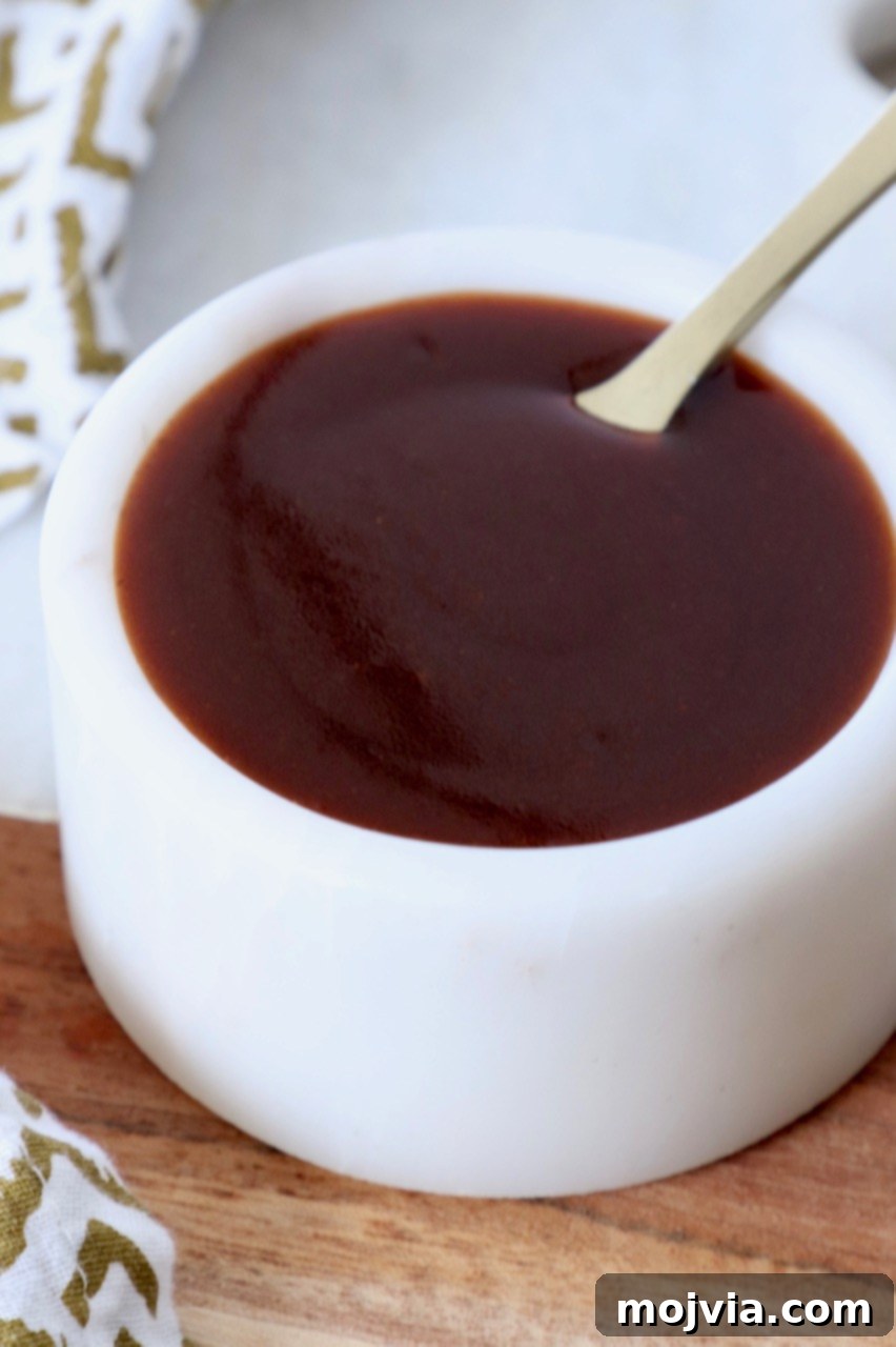 Perfect Stir-Fry Sauce 6 A small white bowl filled with the best homemade stir fry sauce, accompanied by a tiny golden spoon, highlighting its smooth texture and rich color, signifying its readiness for a delicious meal.