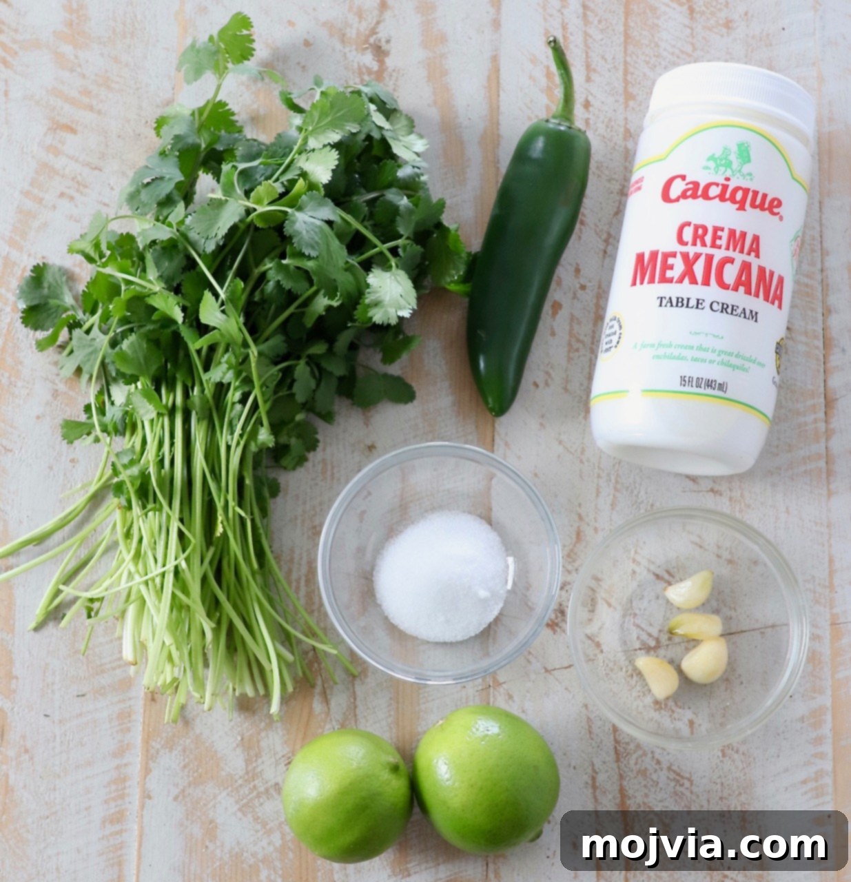 Bright Cilantro Lime Sauce 3 A colorful array of fresh ingredients laid out on a wooden cutting board, including cilantro, limes, a jalapeño, and garlic cloves, for making cilantro lime sauce.