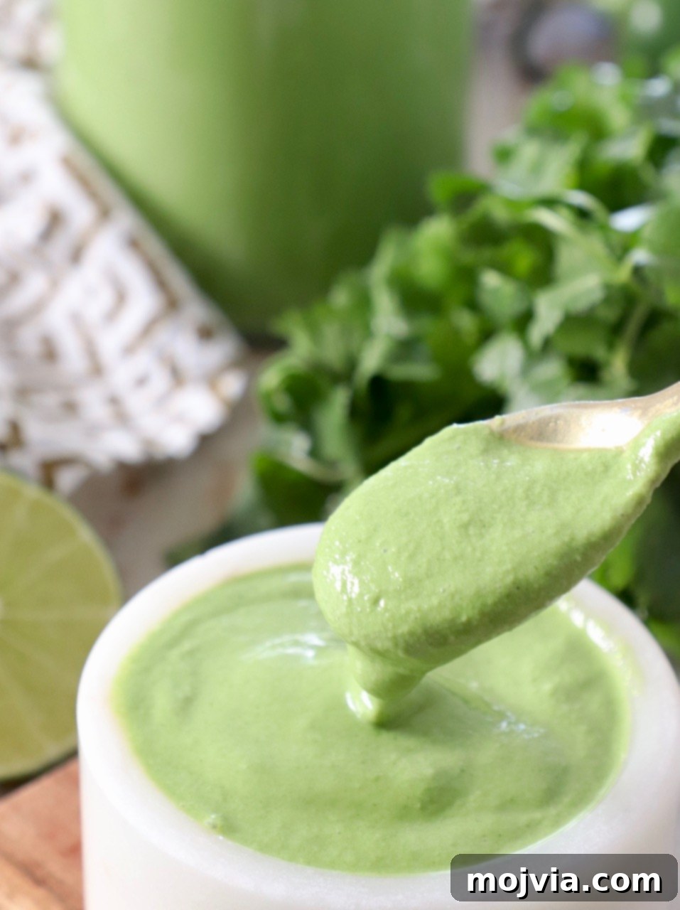 Bright Cilantro Lime Sauce 6 A close-up shot of creamy cilantro lime sauce being scooped onto a spoon from a small white bowl, highlighting its smooth texture.
