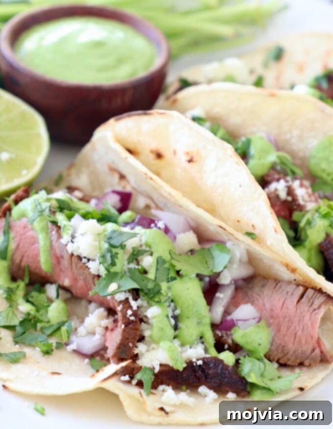 Grilled Steak Tacos on a plate, generously topped with creamy cilantro sauce and fresh cilantro.